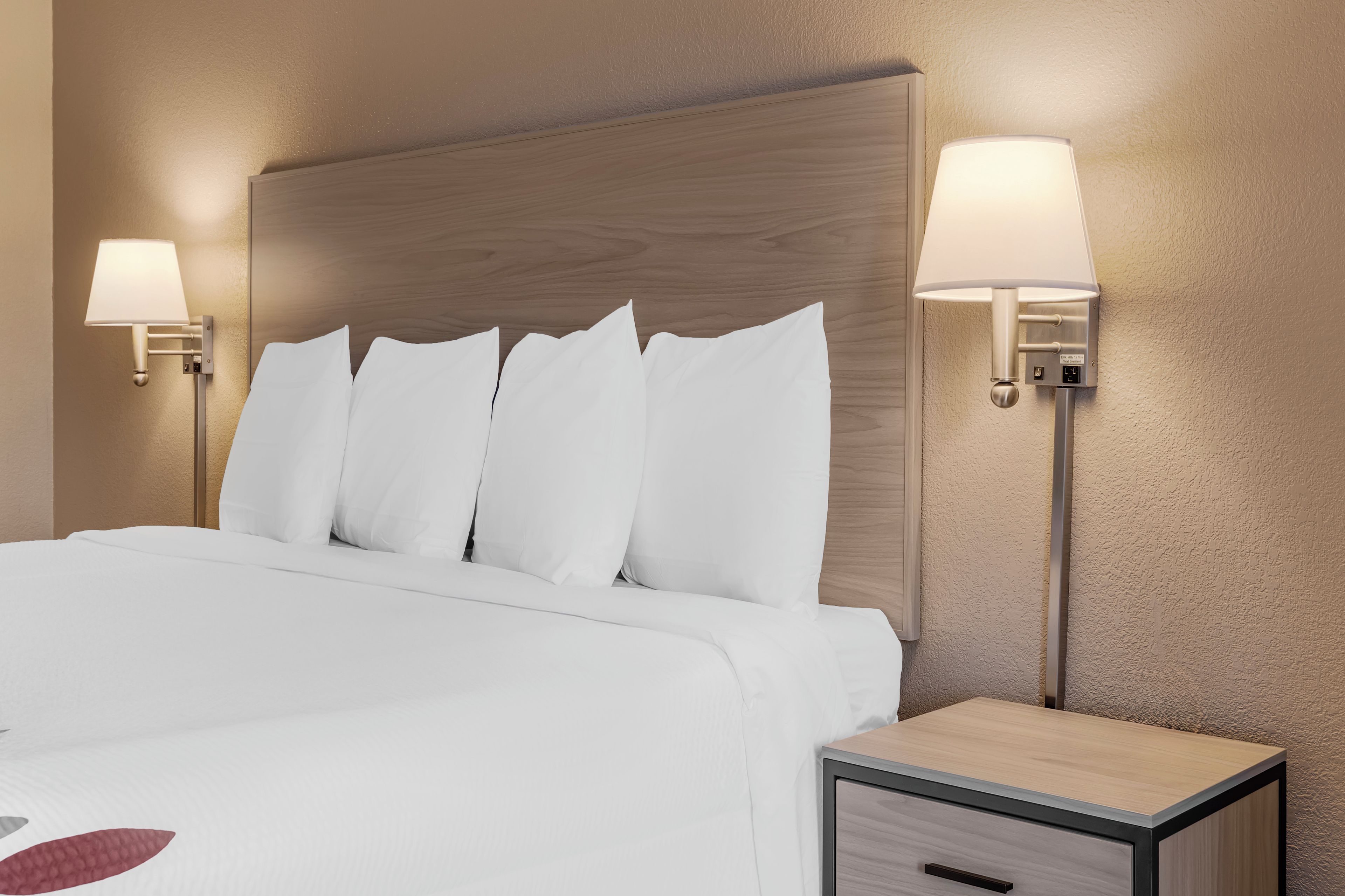 Una habitación de hotel con cabecera de madera, ropa de cama blanca y dos lámparas de noche.