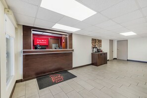 A hotel reception area with a red sign indicating free Wi-Fi in all rooms, a reception desk, a coffee machine, and a door to the Red Roof Inn. - Red Roof Inn Stroudsburg (Stroudsburg)