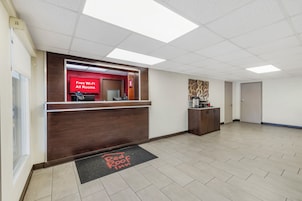 A hotel reception area with a red sign indicating free Wi-Fi in all rooms, a reception desk, a coffee machine, and a door to the Red Roof Inn.