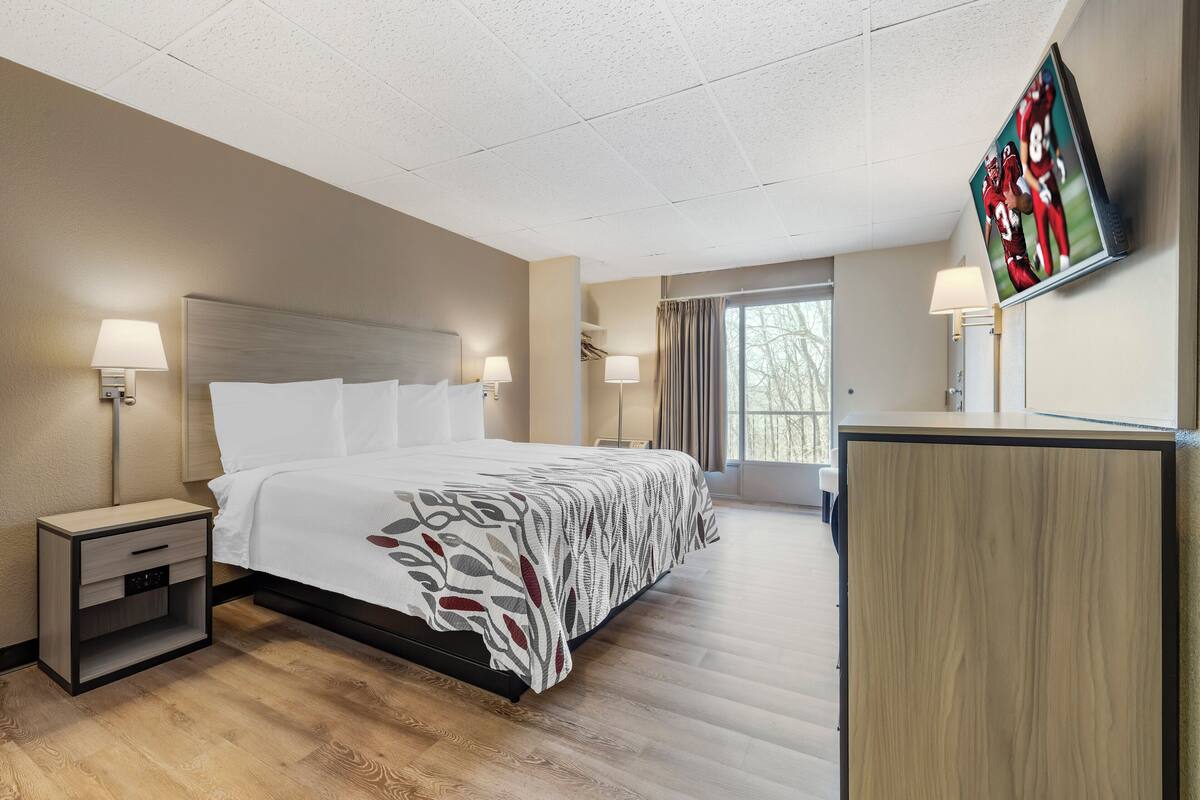 A hotel room with a large bed, two bedside tables, a TV mounted on the wall, and a window with curtains.
