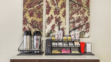 Een koffiehoek met twee koffiezetapparaten, een melkopschuimer en diverse koffiekapsules en roomzakjes.