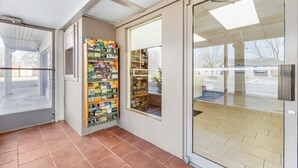 A modern interior with a tiled floor, a glass door leading outside, and a wall-mounted bookcase filled with books. - Red Roof Inn Stroudsburg (Stroudsburg)