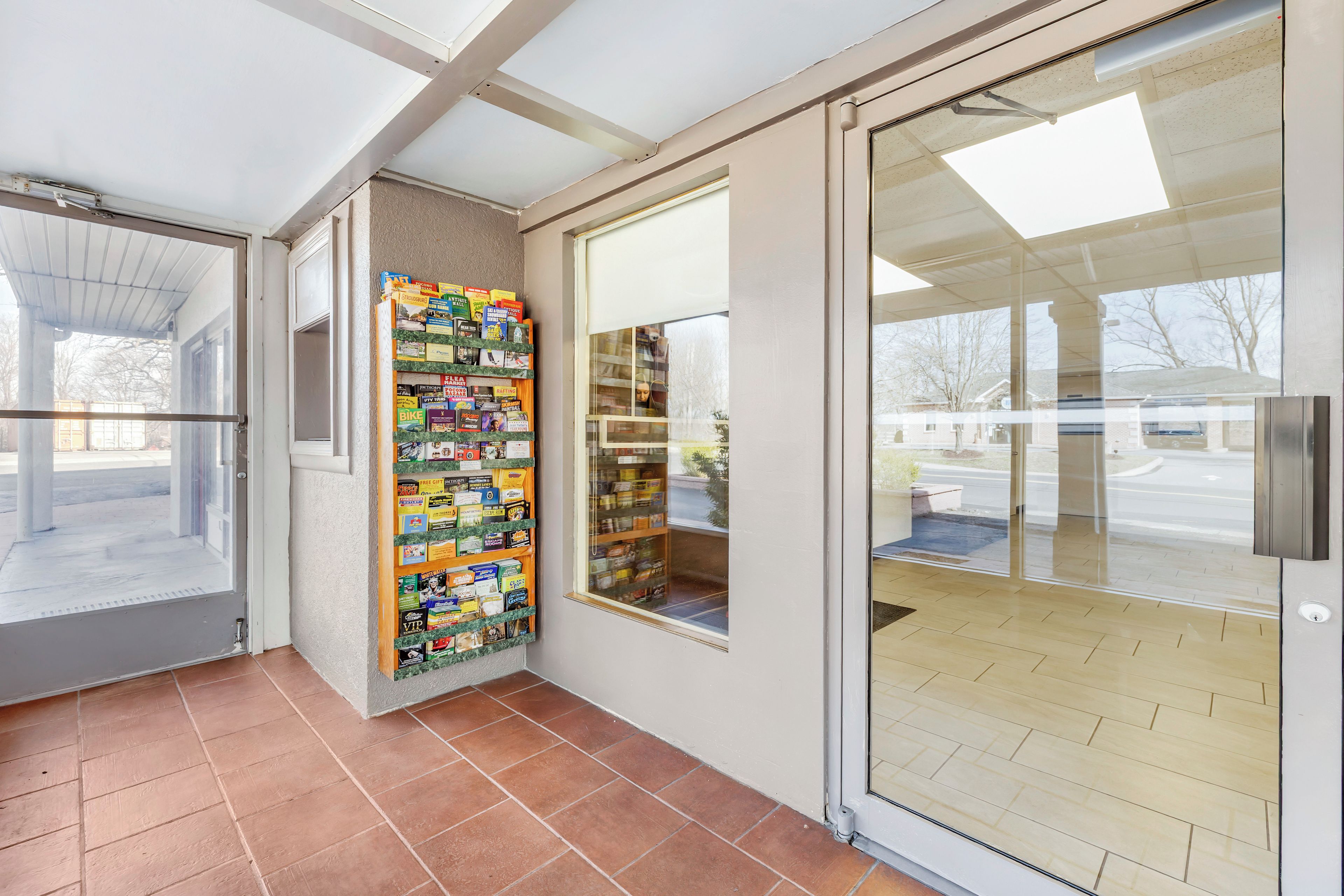 A corner of a room with a tiled floor, a glass door, and a wall-mounted bookcase filled with various books.