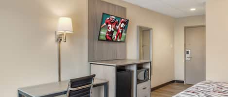 Habitación de hotel con cama, escritorio con silla, televisor montado en la pared, microondas y puerta con cerradura.