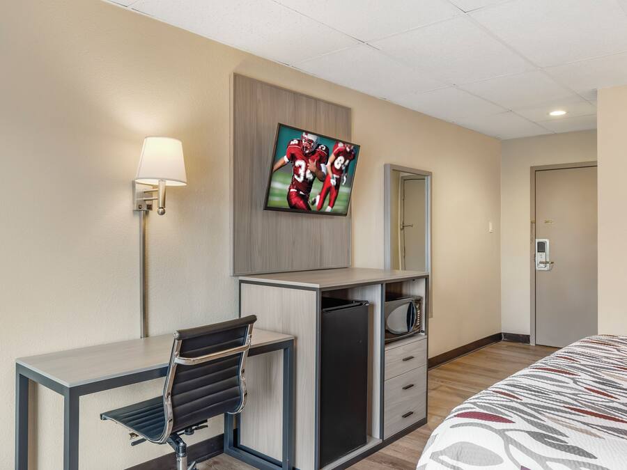 Habitación de hotel con cama, escritorio con silla, televisor montado en la pared, microondas y puerta con cerradura.