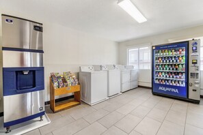 Un cuarto de lavandería con máquinas expendedoras, un refrigerador y un estante de revistas.