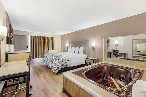 Habitación de hotel con cama, escritorio, silla, un espejo grande, baño con bañera y ducha.