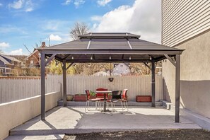 Un patio cubierto con una mesa y sillas, una cerca blanca de piquete y una casa al fondo.