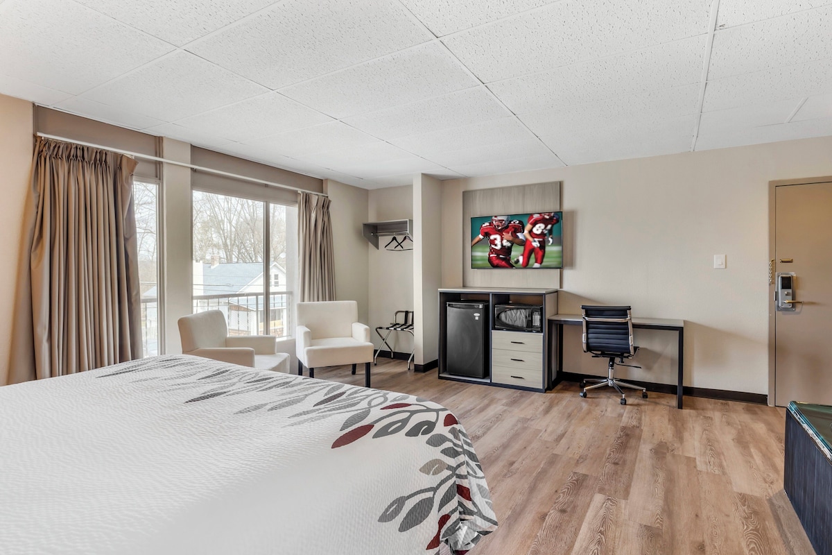 A hotel room with a large bed, a desk with a chair, a television, and a minibar.