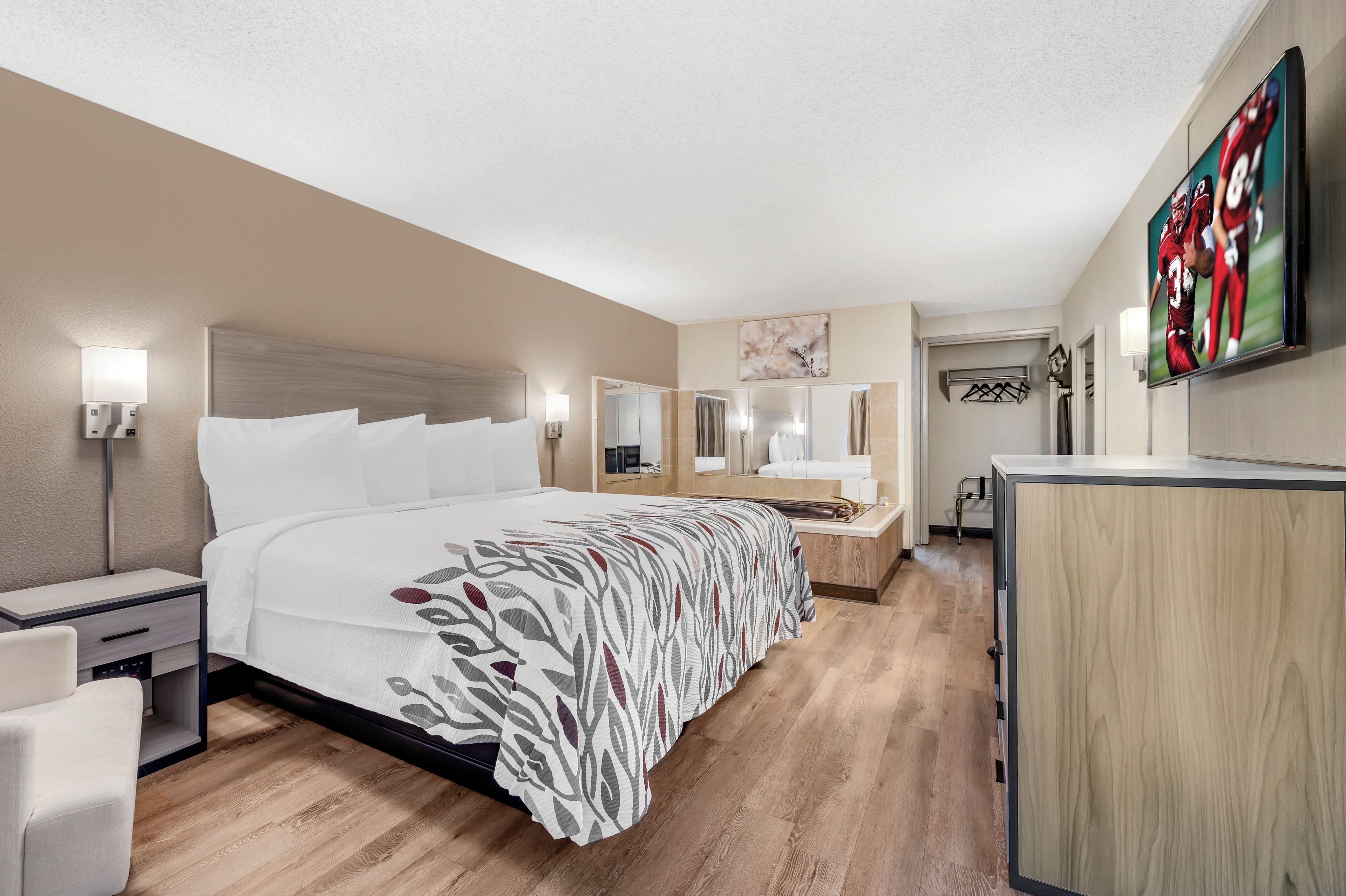 A hotel room with a large bed, bedside tables, a desk, a mirror, and a TV mounted on the wall.