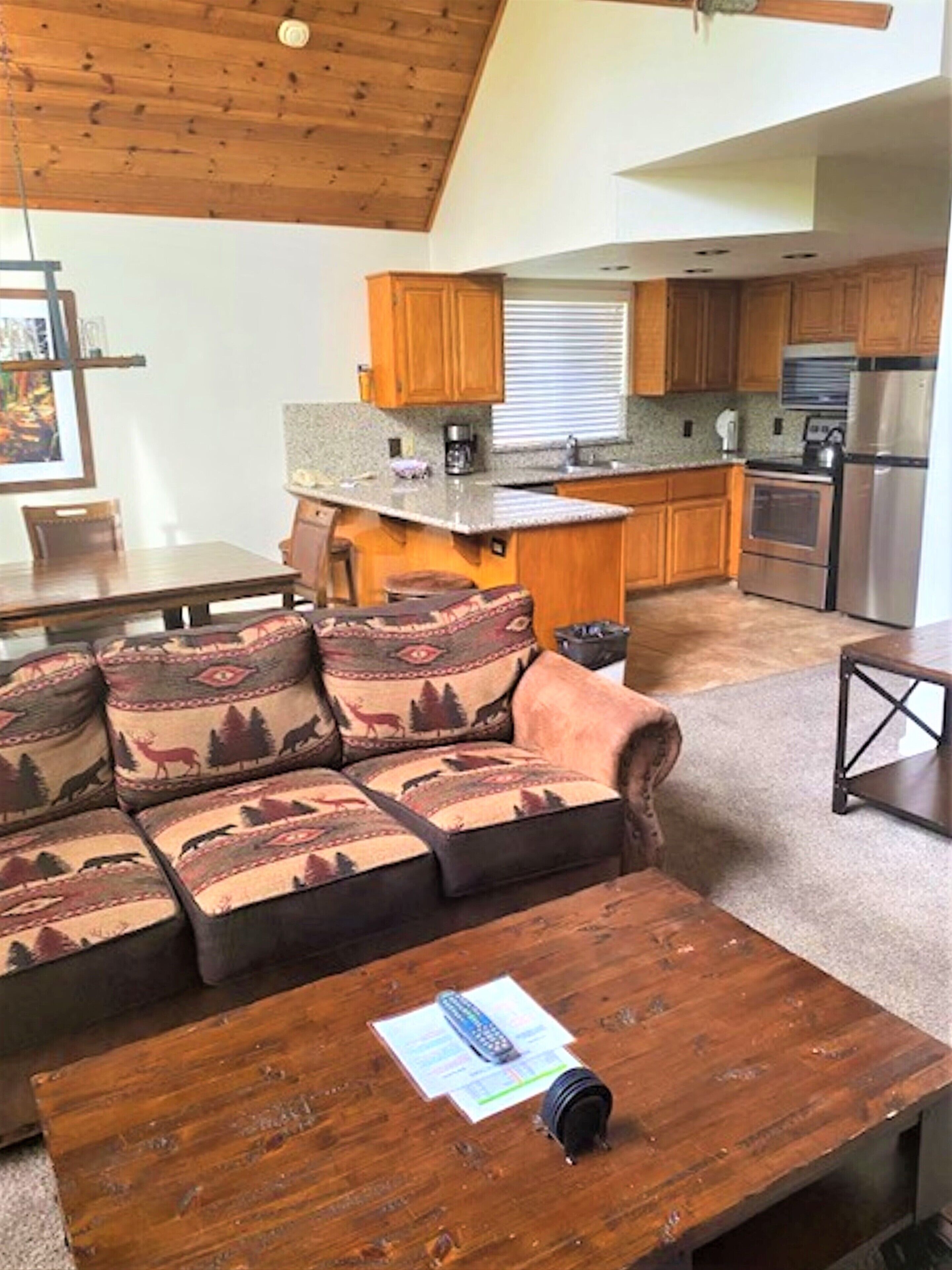 A living room with a sofa, a coffee table, and a kitchen in the background.