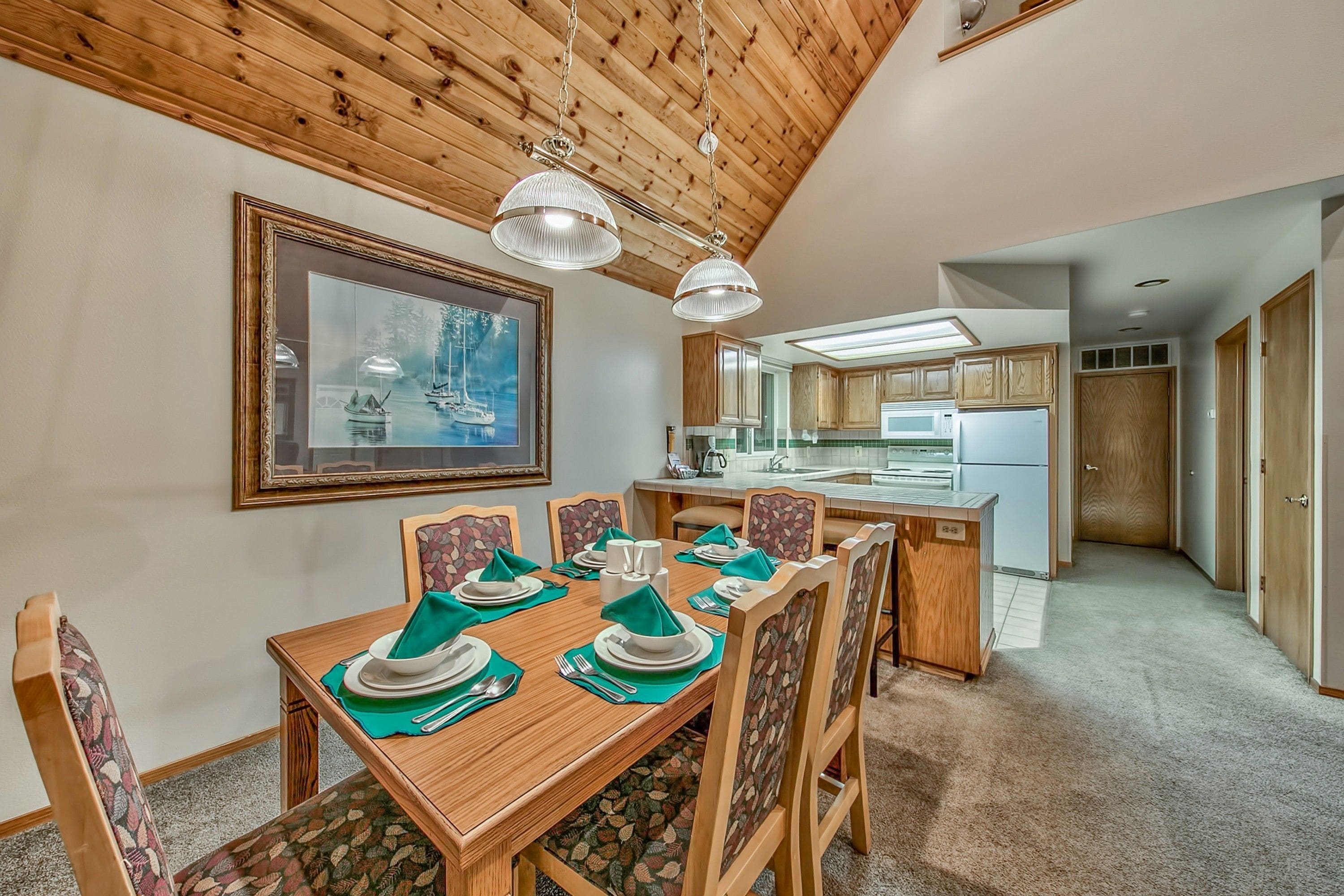 A dining area with a wooden table set for six, wooden chairs, and a framed picture on the wall.
