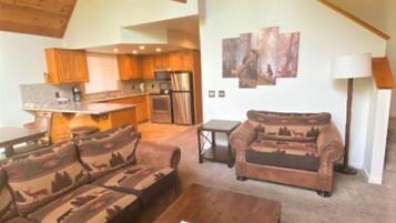 A spacious living area with a large sofa set, a wooden coffee table, and a kitchen in the background.