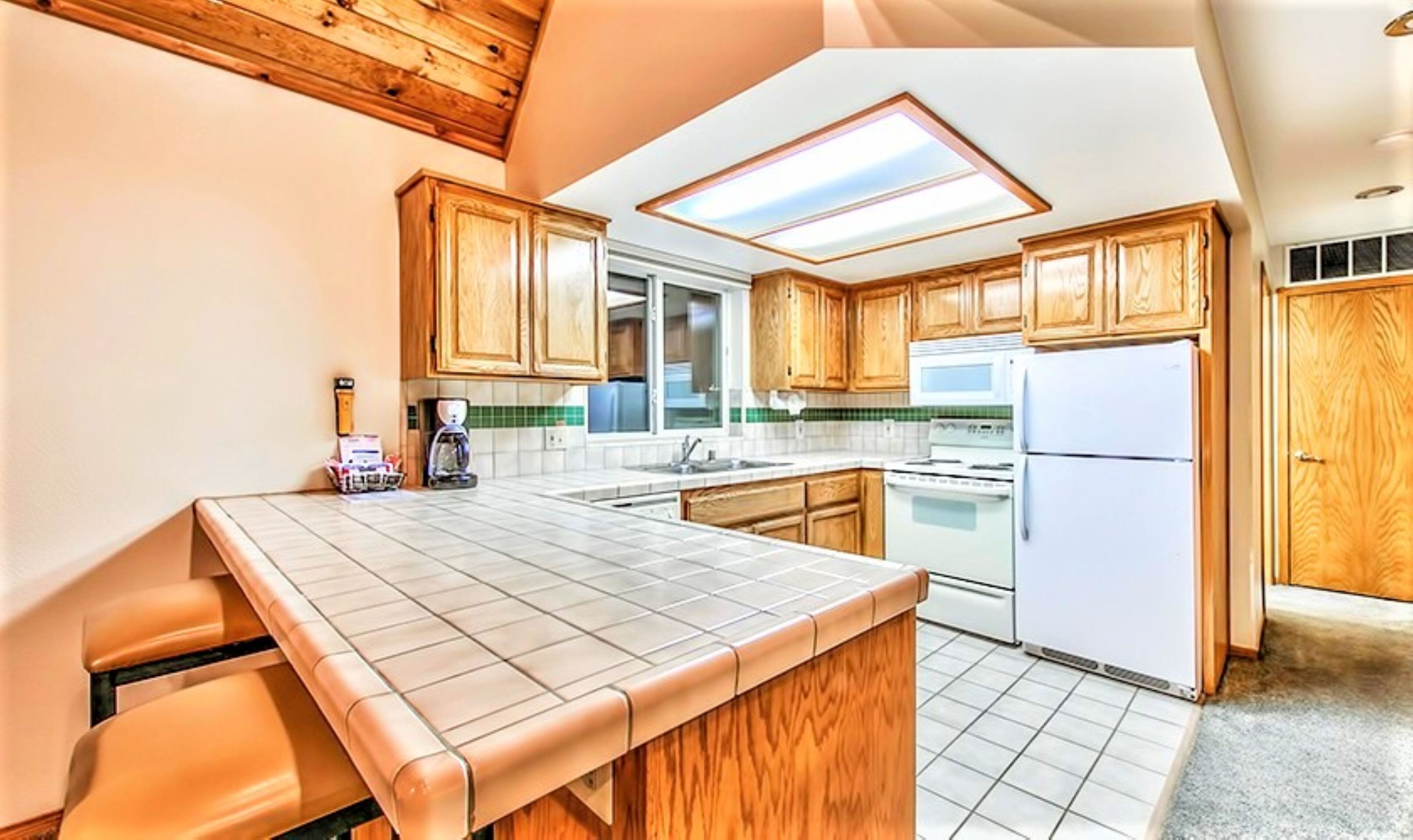 A kitchen with wooden cabinets, a white refrigerator, a stove, and a window with skylight.
