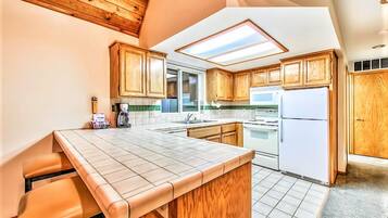 A kitchen with wooden cabinets, a white refrigerator, a stove, and a window with skylight.