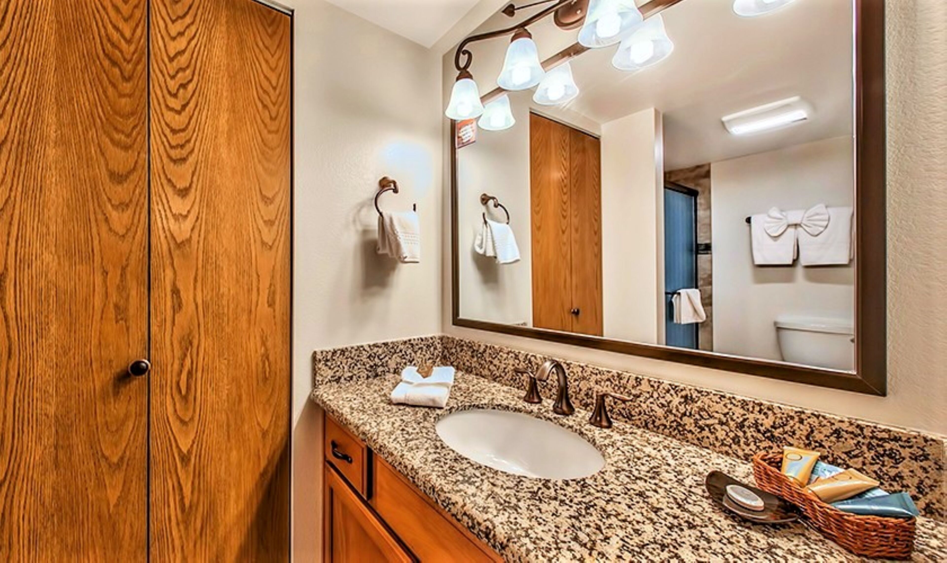 A bathroom with a wooden door, a granite countertop, a sink, a mirror, and a wall-mounted towel rack.