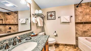 A bathroom with a granite countertop sink, a toilet, and a bathtub.