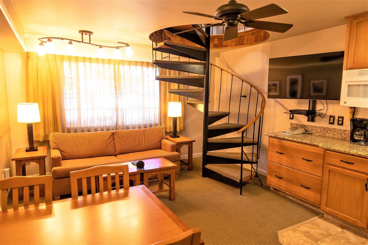 Una habitación de hotel compacta con una escalera de caracol, un sofá, una mesa de comedor y una zona de cocina.