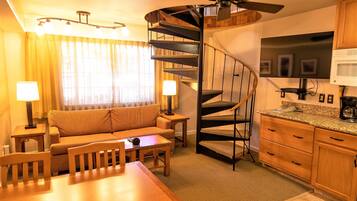 Een compacte hotelkamer met een spiltrap, een bank, een eettafel en een keukenhoek.