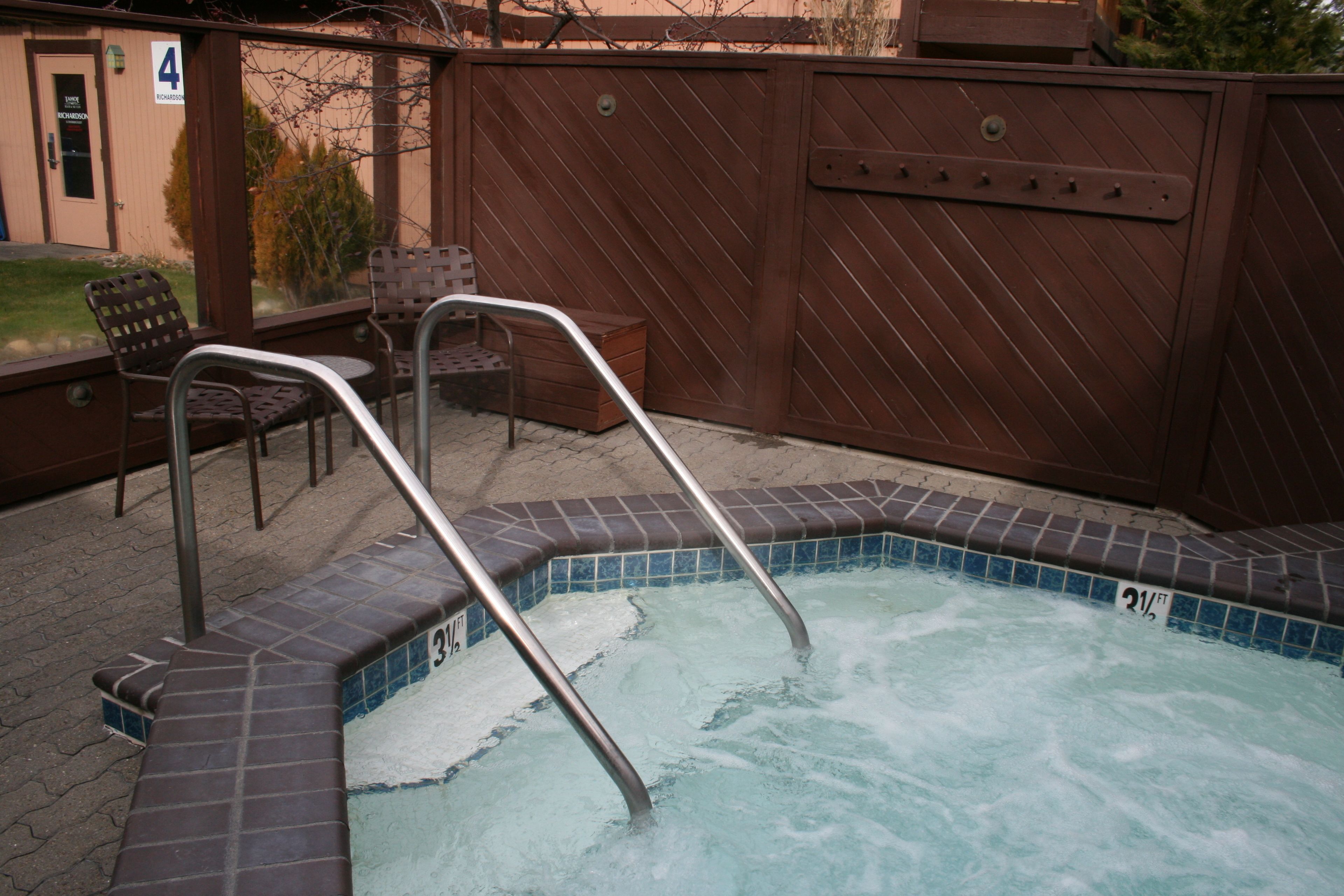 Ein Whirlpool mit Metallstufen und einer gefliesten Kante, ein Holenzaun und eine Bank im Hintergrund.