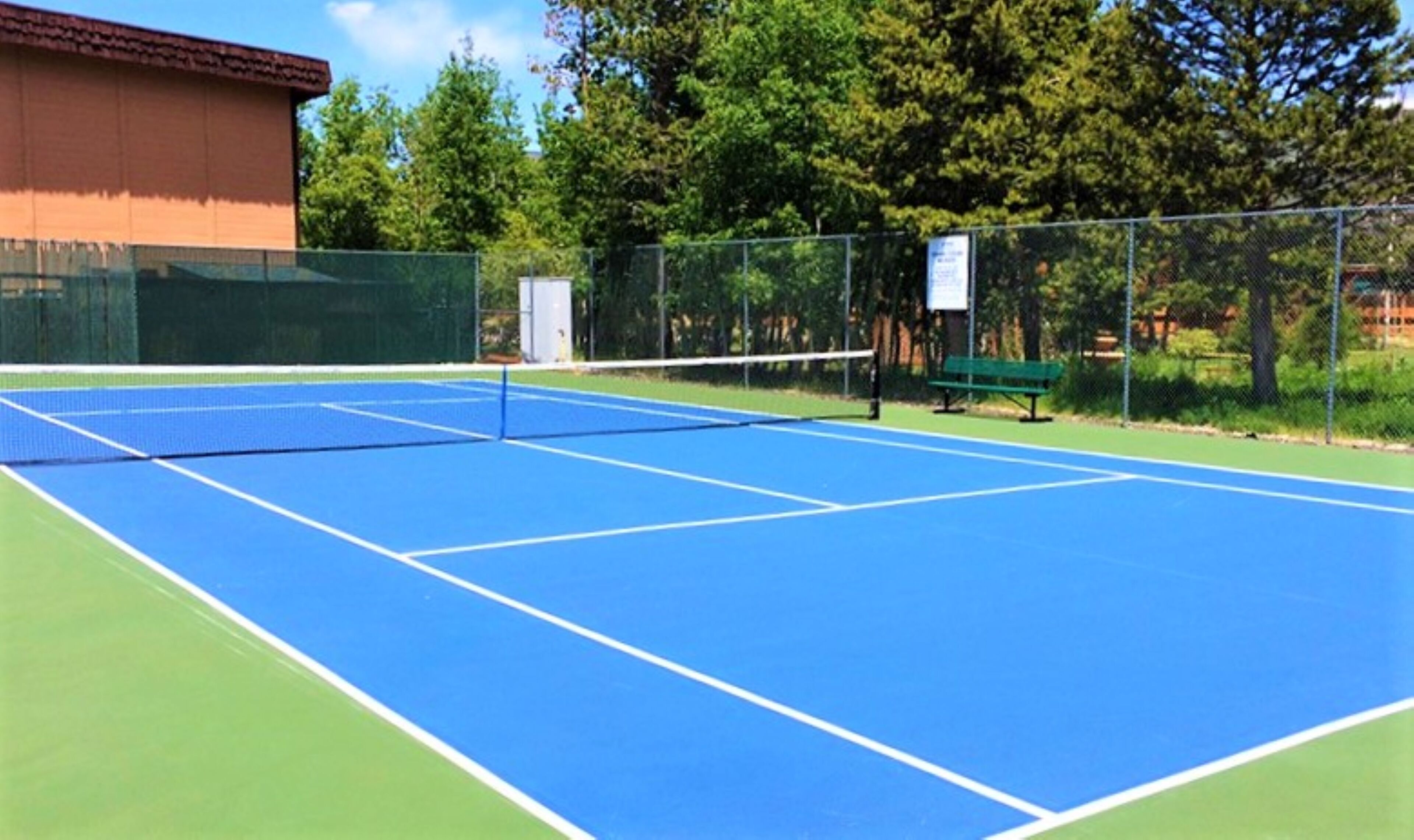 A tennis court with a net, surrounded by a fence and trees.