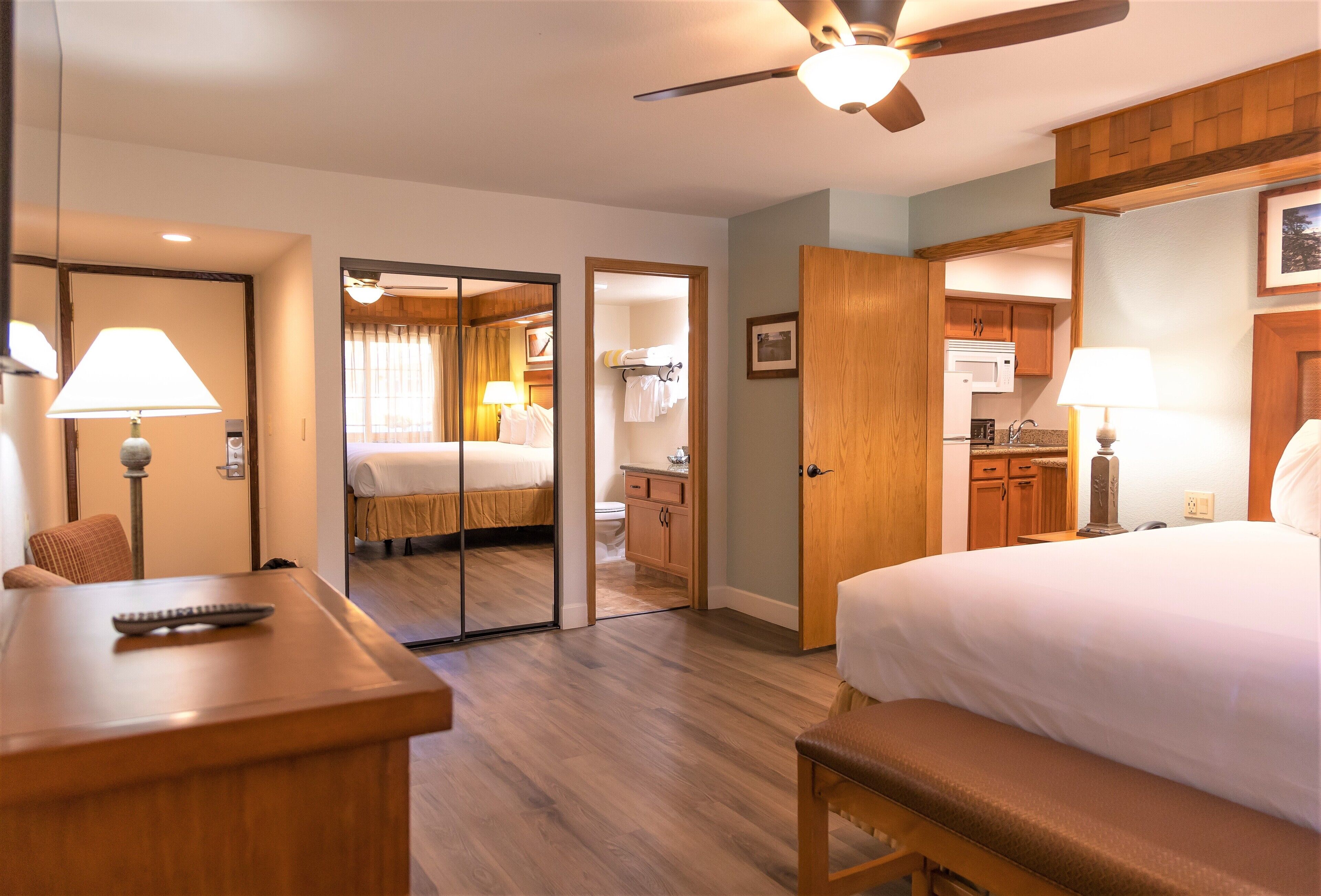 Quarto de hotel com cama, mesa de cabeceira, luminária e vista para o banheiro e cozinha.