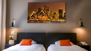 A hotel room with two beds, a cityscape painting, and a night view of a city skyline. - Atlas Hotel Brussels (Brussels)