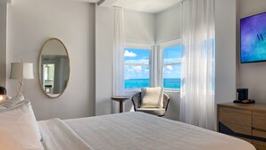 Een hotelkamer met een groot bed, een stoel bij het raam, een tafeltje, een spiegel, een televisie en een koffiezetapparaat.