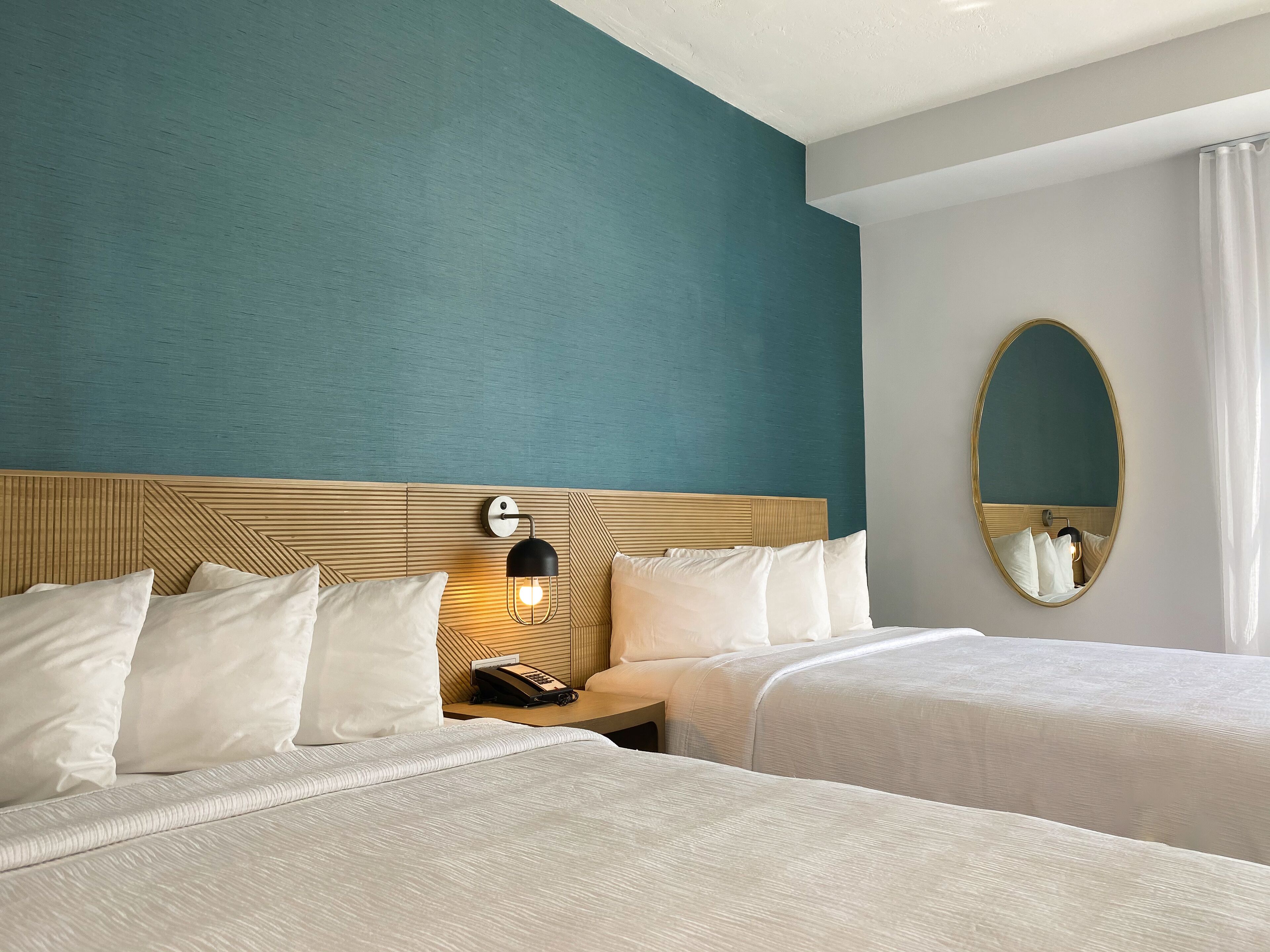 A hotel room with two beds, a wooden headboard, a wall-mounted light, a telephone, and a mirror.