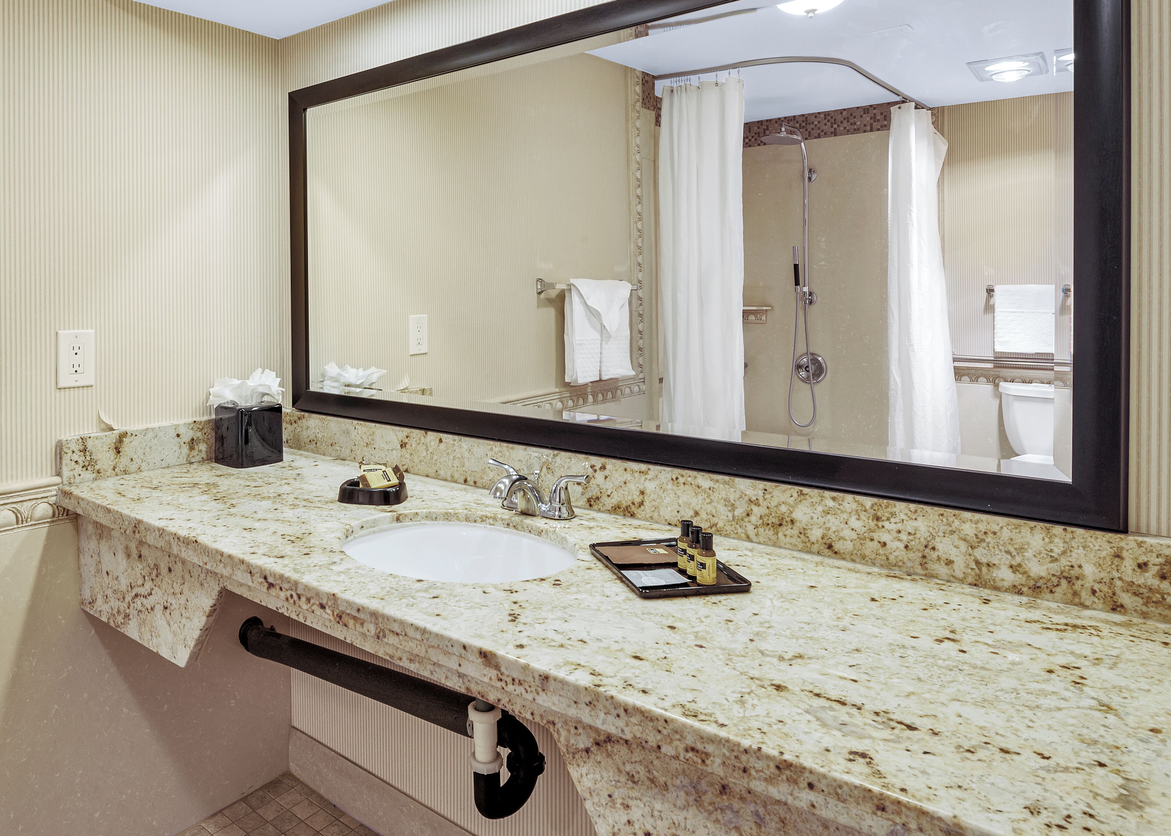 A bathroom with a large mirror, a sink, a shower, and a towel rack.