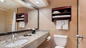 A bathroom with a granite countertop sink, a mirror, a toilet, and two towel racks.