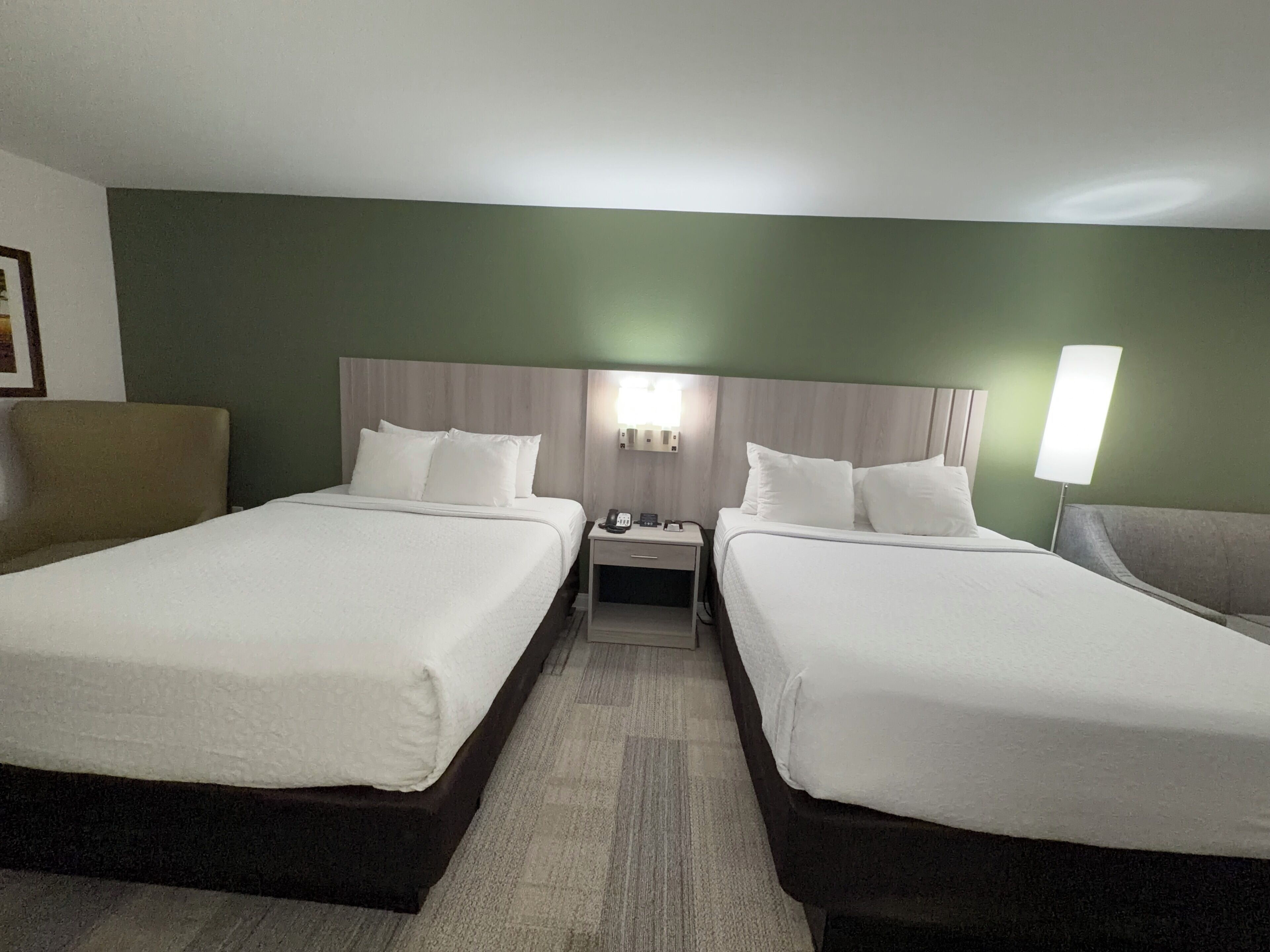 Habitación de hotel con dos camas, una mesita de noche, una lámpara y una silla.