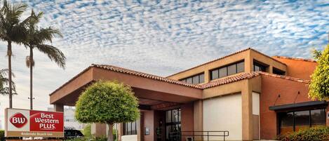 Un hotel Best Western Plus con tejado de tejas rojas, palmeras y una entrada ajardinada.