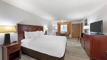 A hotel room with a large bed, bedside tables, a desk with a chair, a television, and a wardrobe.