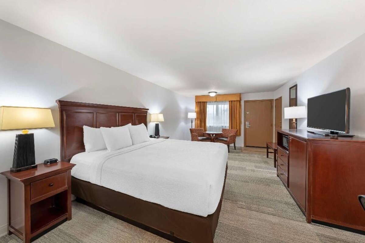 A hotel room with a large bed, bedside tables, a desk, a chair, a television, and a wardrobe.