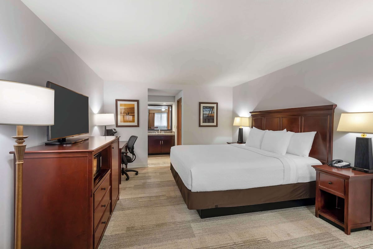 A hotel room with a large bed, a desk, a chair, a television, and a desk lamp.