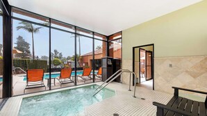 An indoor pool area with clear glass walls, a hot tub, and orange chairs. - Best Western Plus Redondo Beach Inn (Redondo Beach)