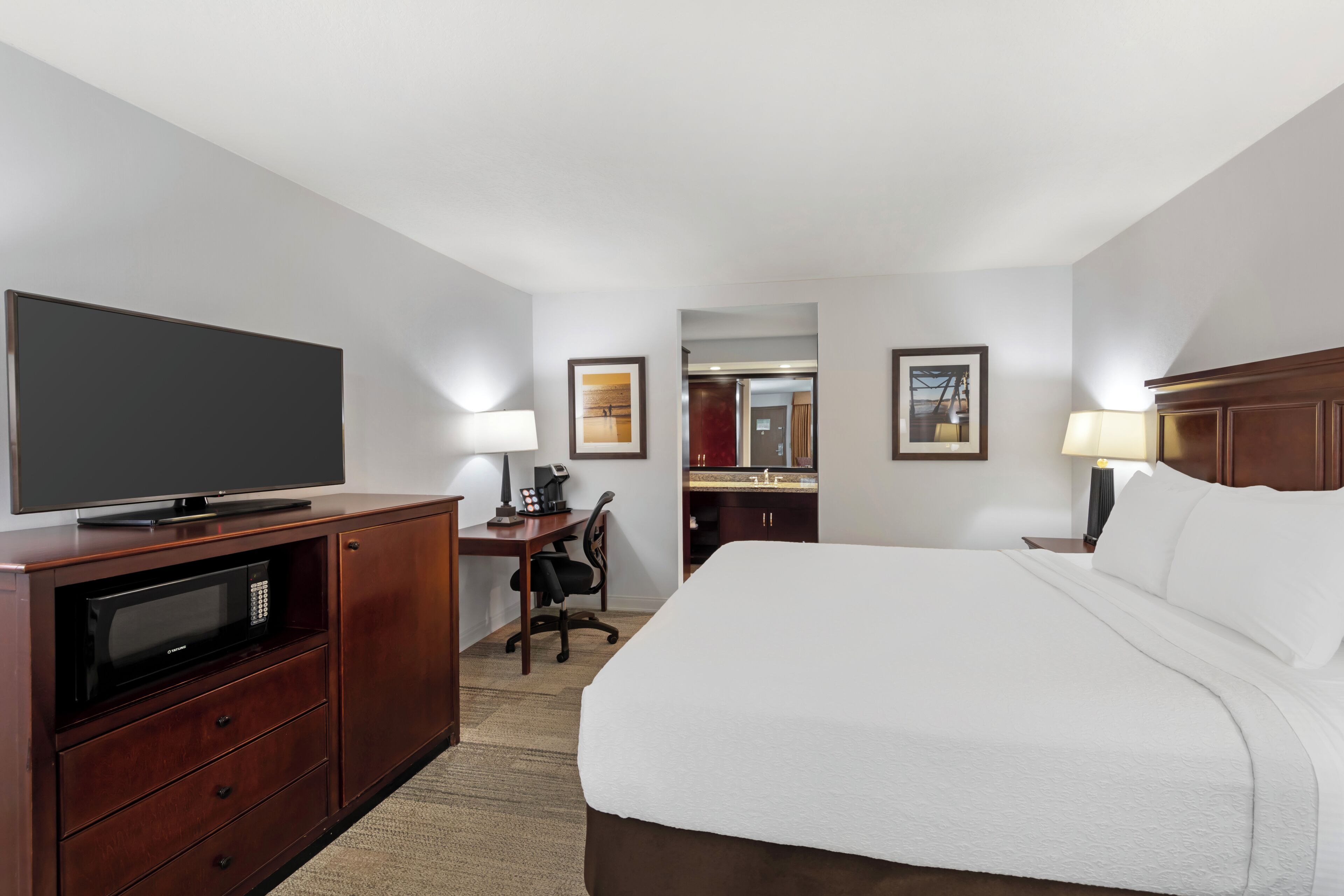 Habitación de hotel con cama, escritorio con computadora, televisor, microondas y baño visible a través de una puerta abierta.