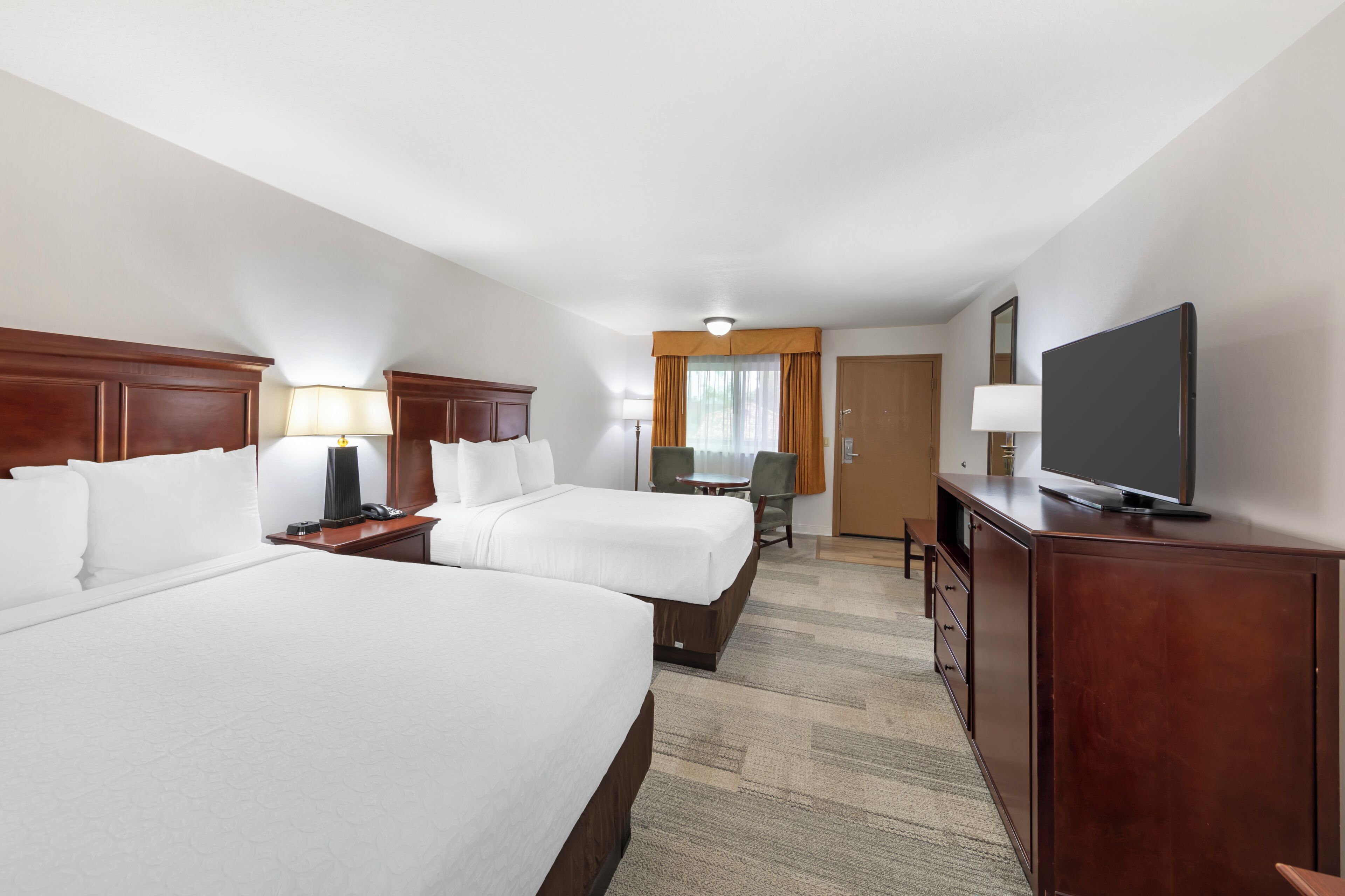 A hotel room with two beds, a desk, a chair, a television, and a door.