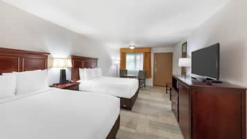 A hotel room with two beds, a desk, a chair, a television, and a door.