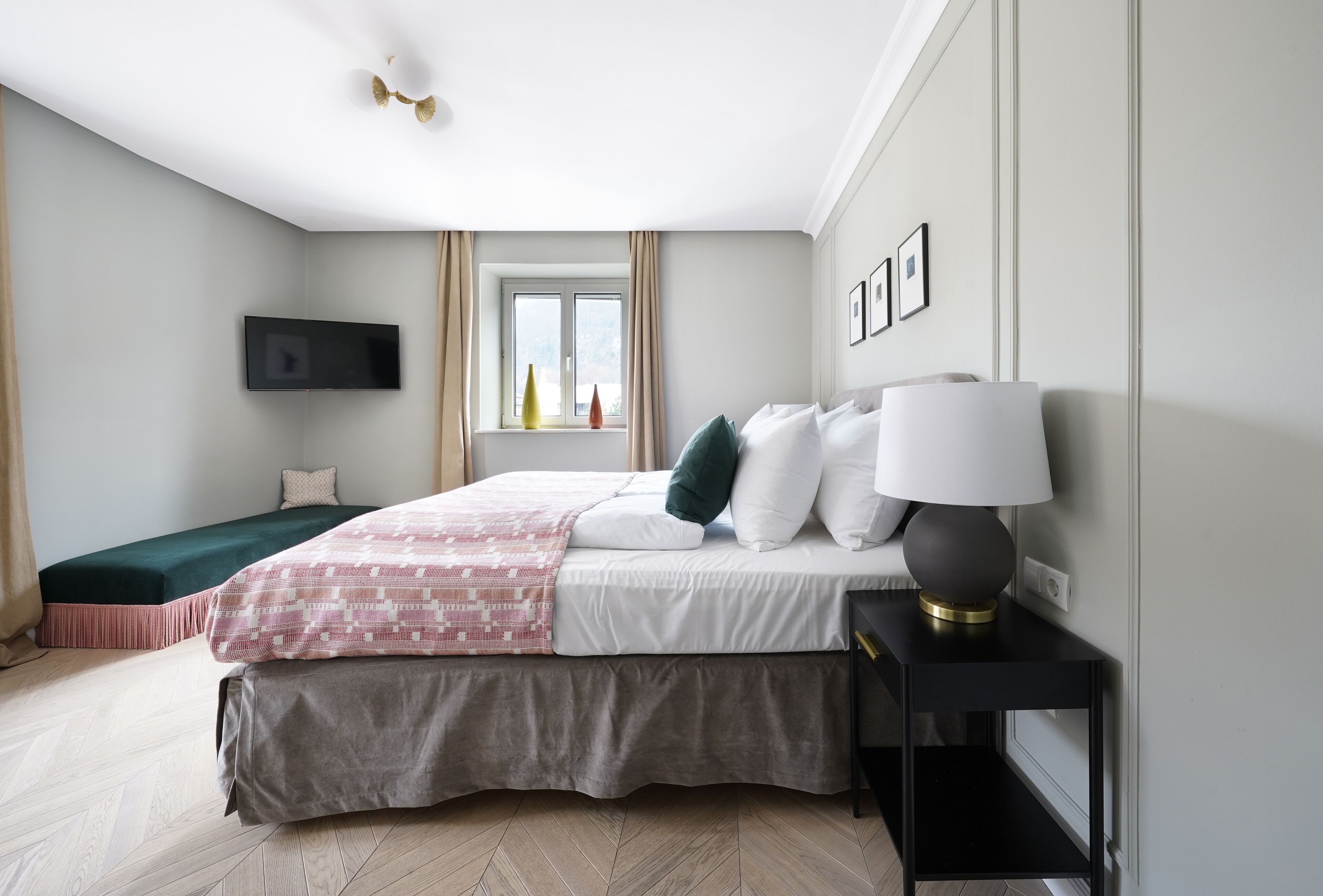 Ett modernt hotellrum med en stor säng, ett nattduksbord med en lampa, en platt-TV som är monterad på väggen och ett fönster med gardiner.