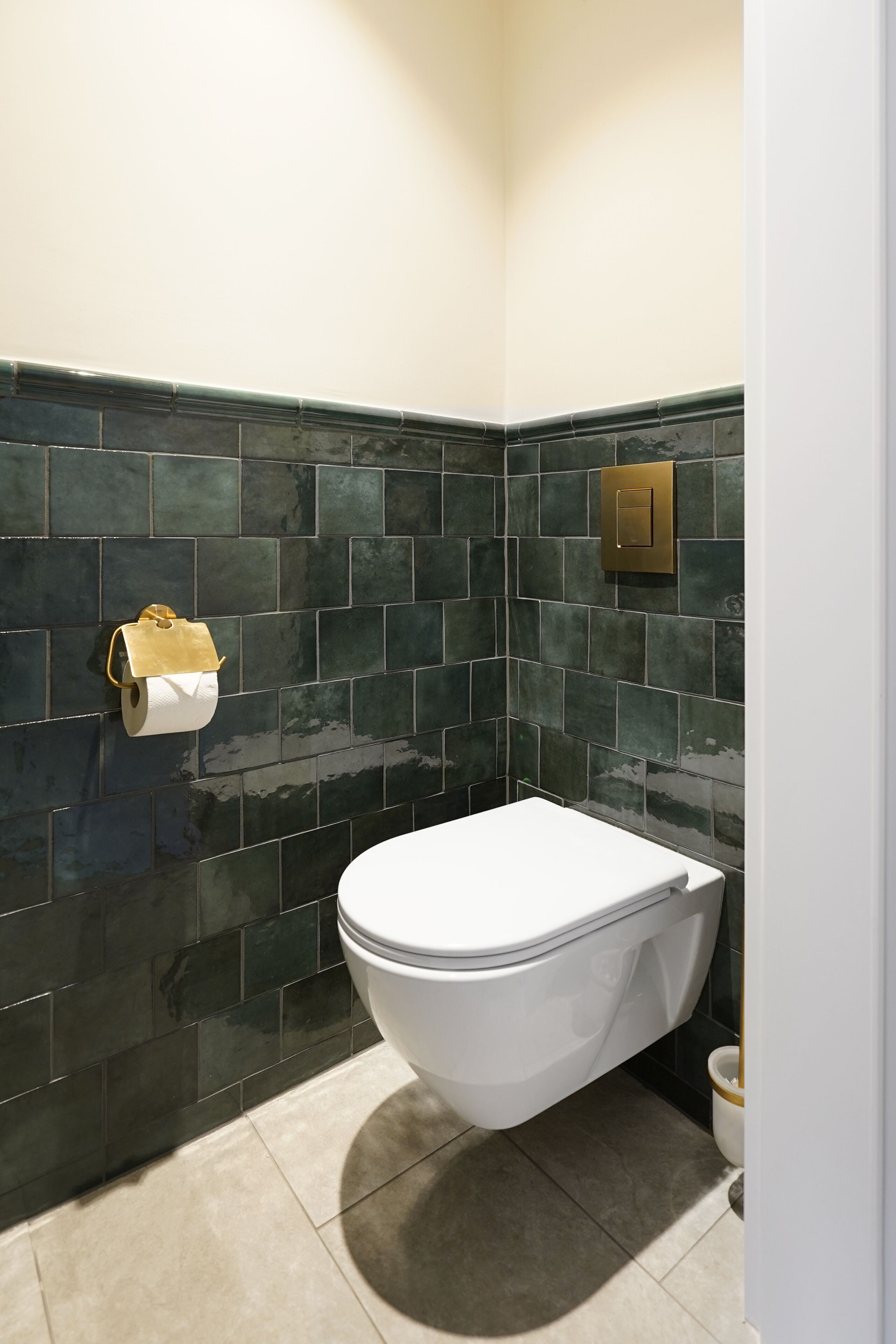 Un baño con inodoro, paredes cubiertas de azulejos verde oscuro y dispensador de papel higiénico.
