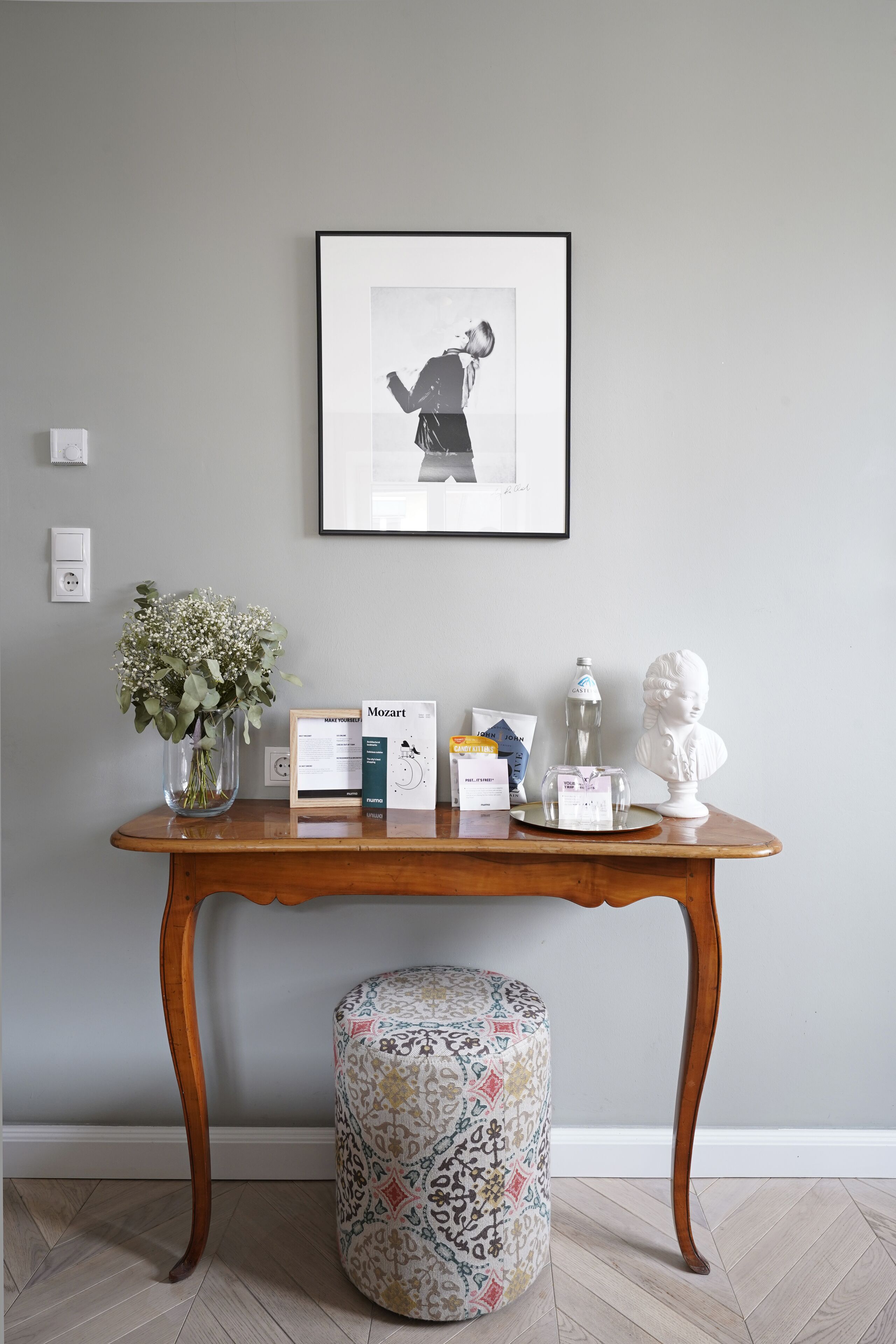 A wooden table with a vase of flowers, a framed picture, and some items on it.