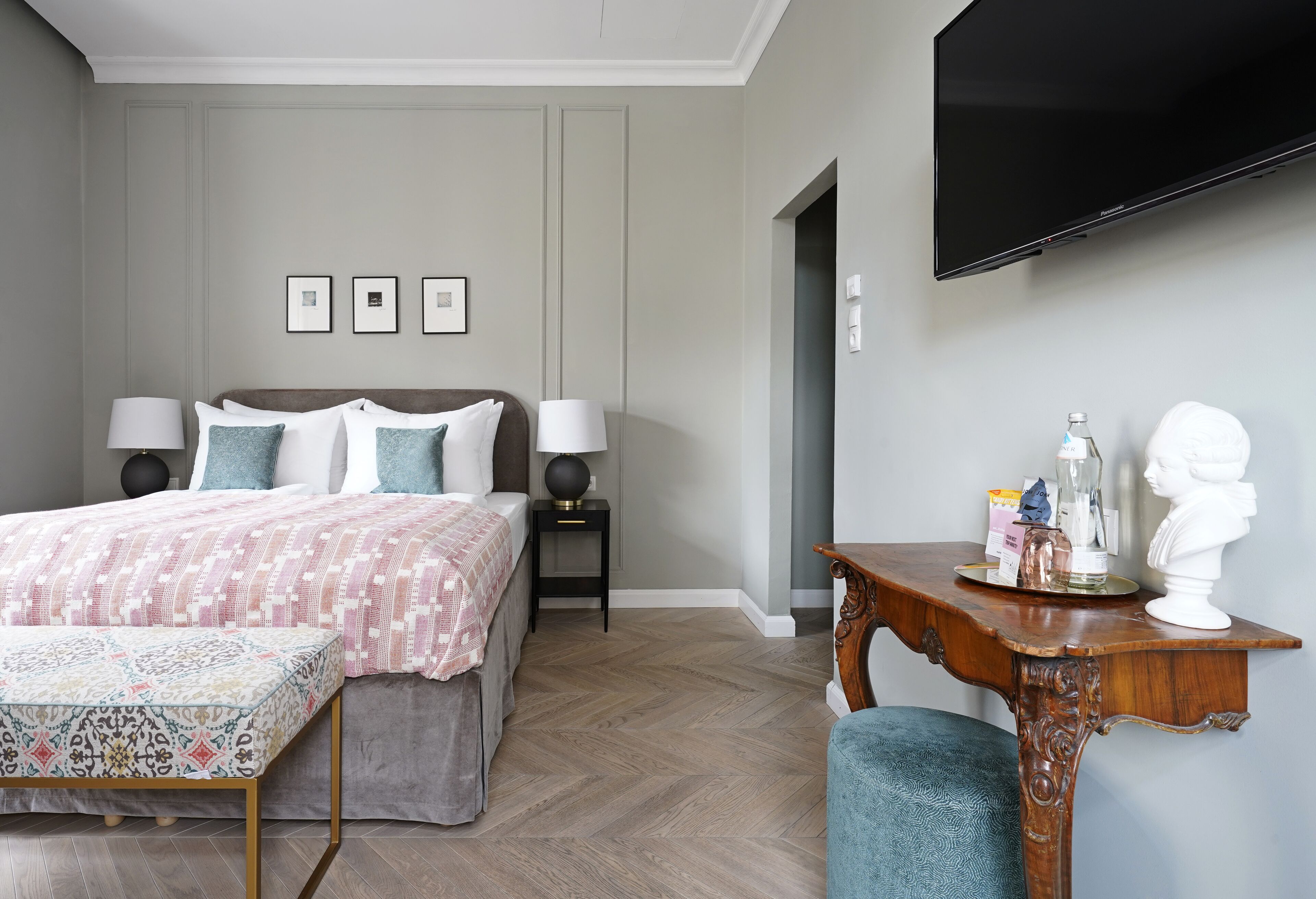 A bedroom with a bed, bedside tables, a TV, and a desk with a bust sculpture.