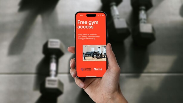 A hand holding a smartphone displaying a message about free gym access at Anytime Fitness during a Numad stay. - Numa Salzburg Mozart (Salzburg)