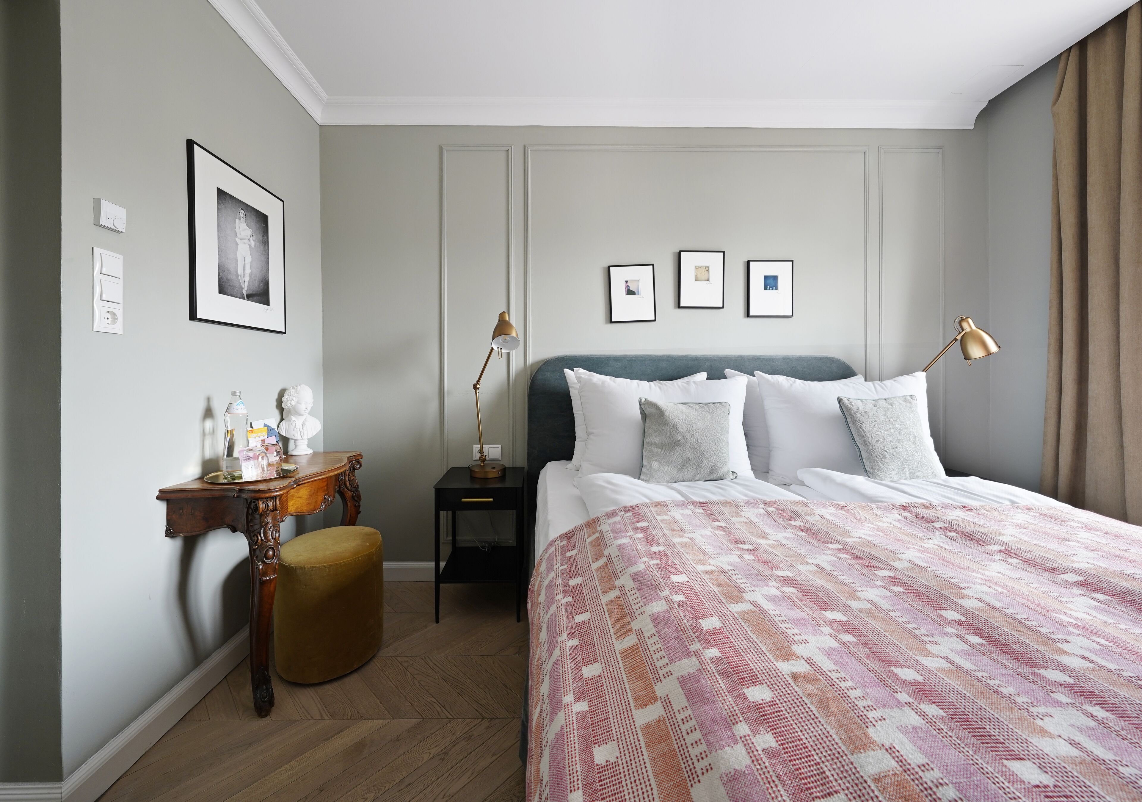 A hotel room with a large bed, a nightstand, a small table with a lamp, and a picture on the wall.