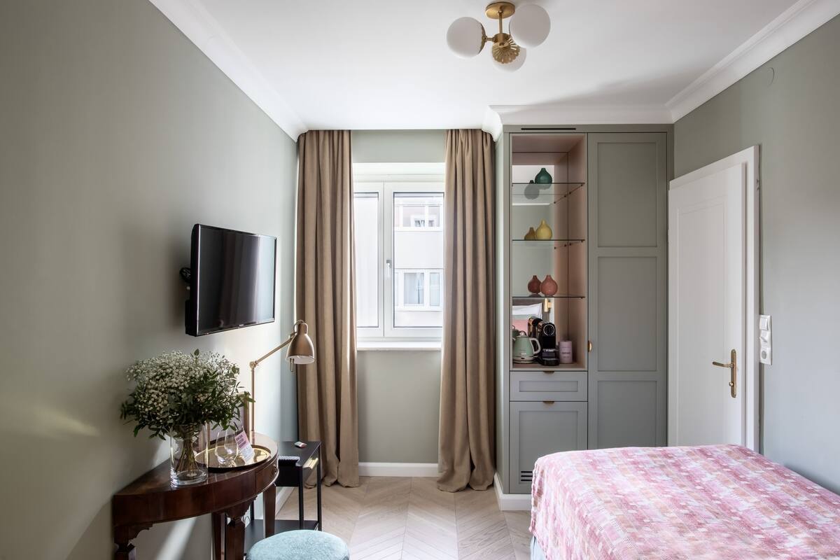 Quarto com cama, escrivaninha com luminária, televisão e guarda-roupa.