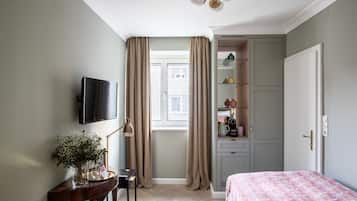 A bedroom with a bed, a desk with a lamp, a TV, and a wardrobe.