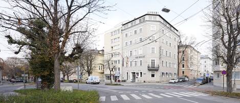A multi-story building with a corner entrance, a crosswalk, and parked cars.