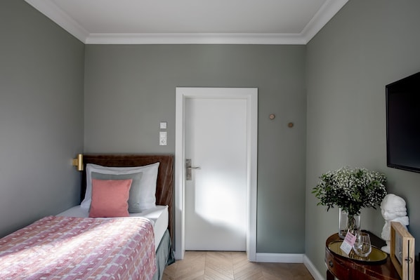 Un dormitorio con una cama, una mesita de noche con un florero y una puerta.